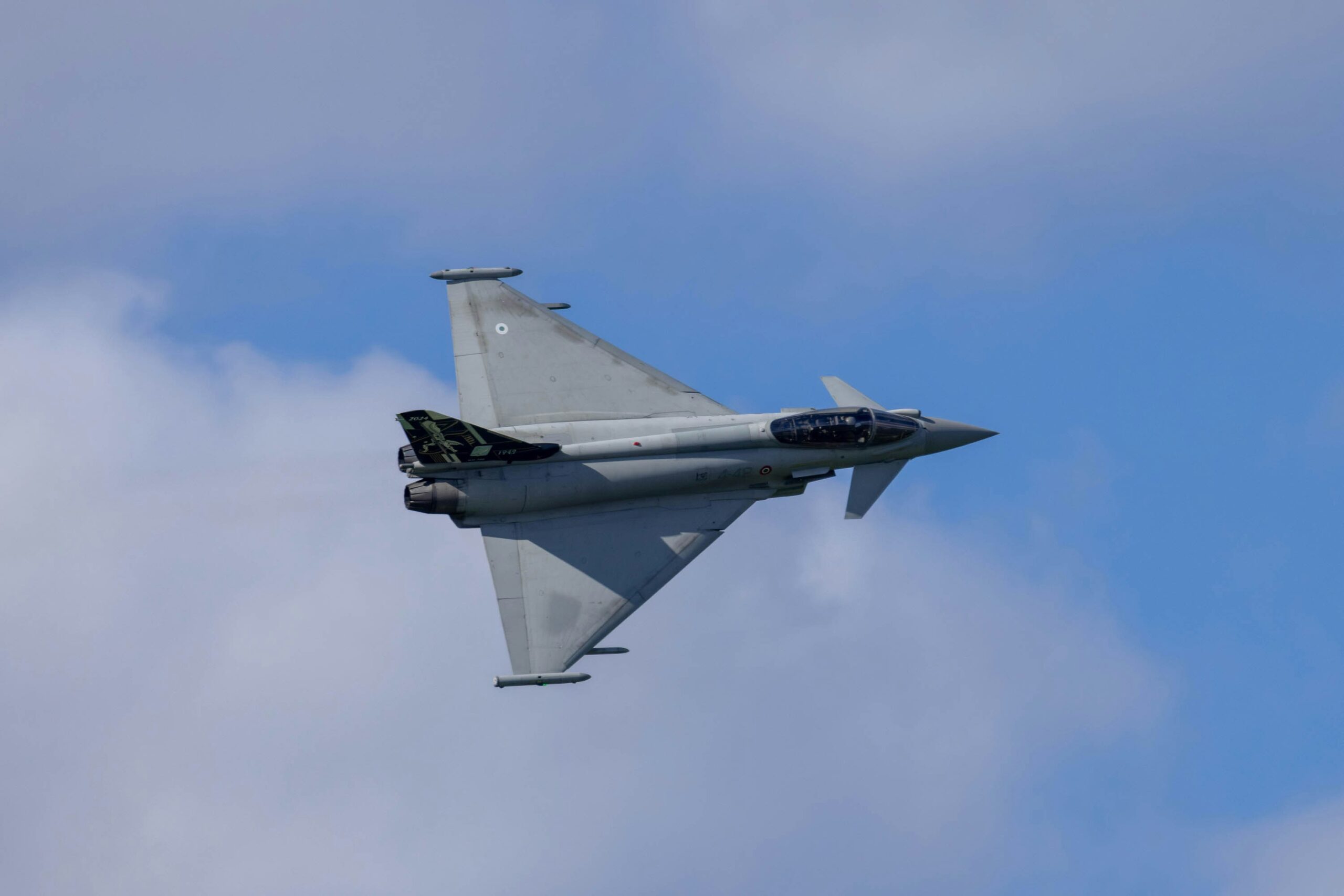 A fighter jet flying through a cloudy blue sky